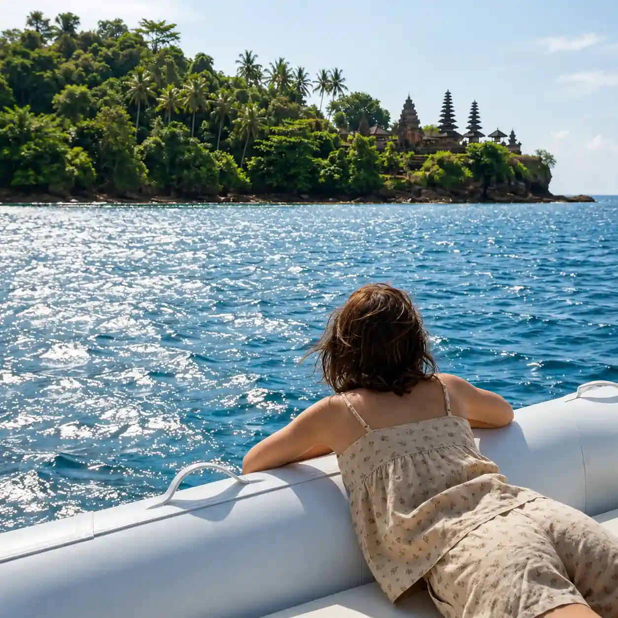 A woman in a lightweight floral cotton dress relaxing on a boat, looking out over calm blue water with a tropical island in the background, capturing the ease of a lake weekend getaway.