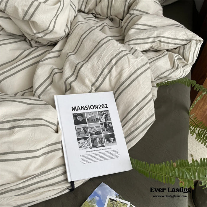 Striped neutral bedding with a soft crumpled look and an open zine on top.